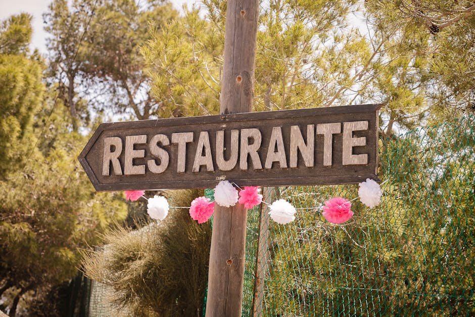 A rustic wooden restaurant sign in Spain, adorned with festive pink and white decorations amidst a natural outdoor setting