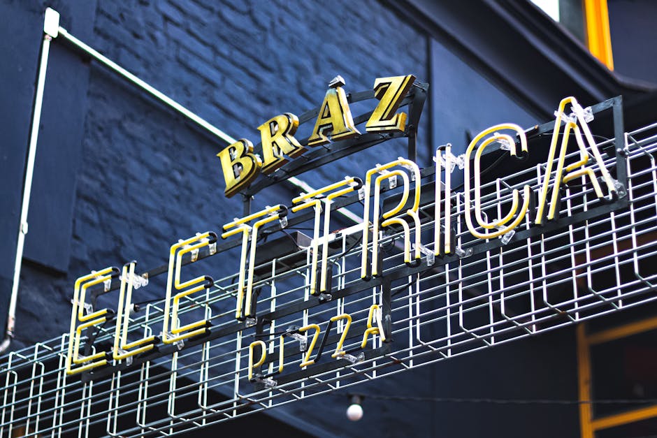 A vibrant neon sign displaying 'Elettrica' at a pizza restaurant, captured outdoors with a striking low angle