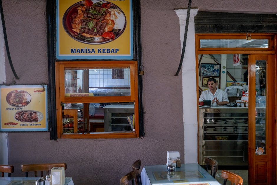 Cozy indoor view of a Turkish restaurant with Manisa kebab posters and a waiter at the counter
